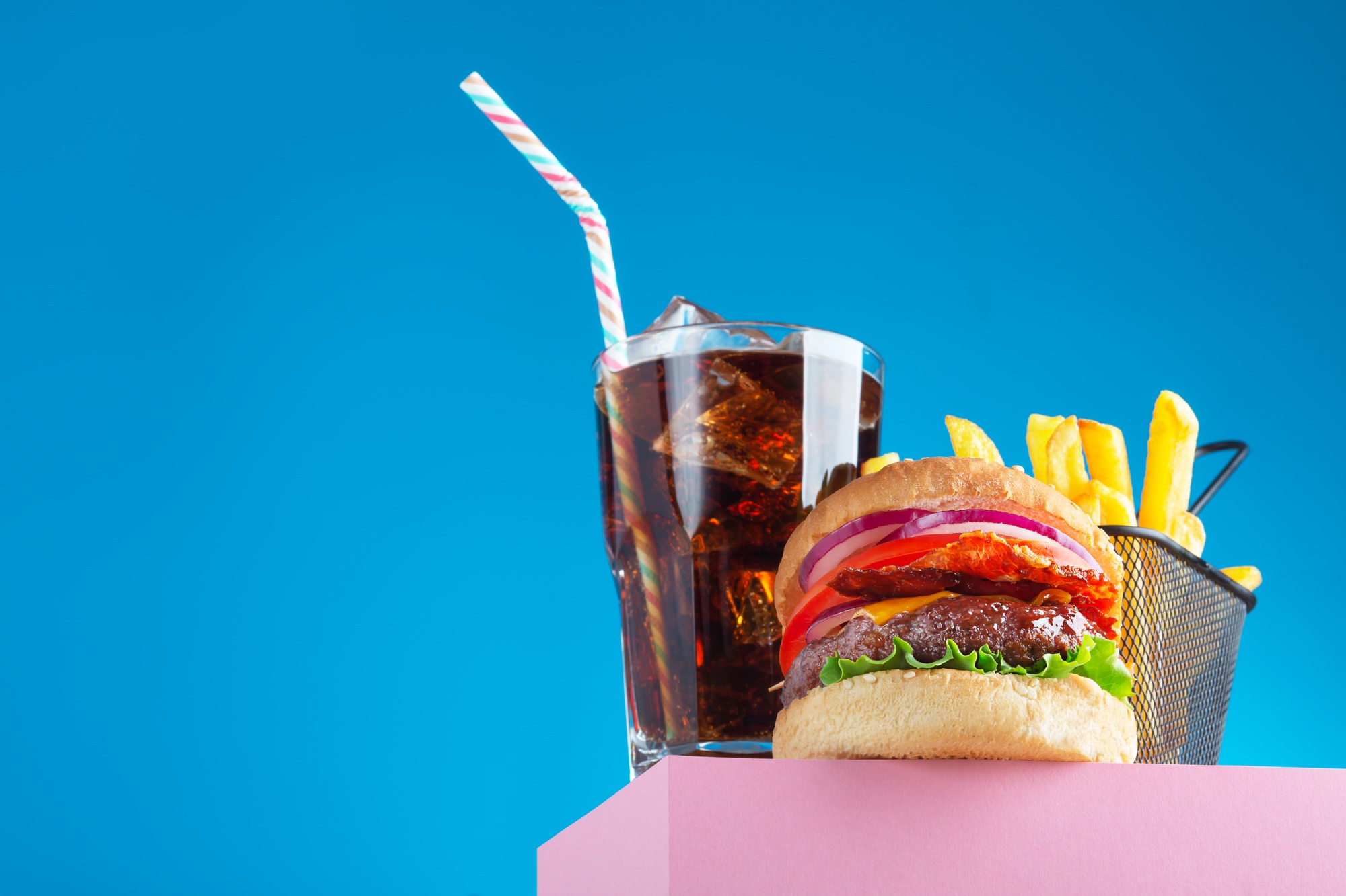 Fresh juicy beef hamburger, fried potatoes and drink, placed on the stand and blue background